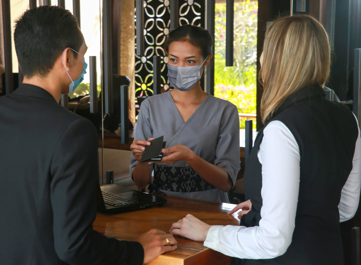 wearing medical masks as precaution against virus. Young couple on a business trip doing check-in at the hotel